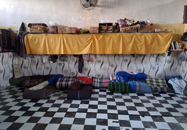 Makeshift sleeping arrangements with yellow tarp divider showing cramped living conditions and lack of proper bedding infrastructure