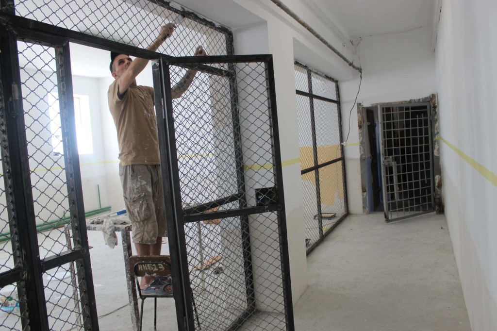 A prisoner standing on a chair to paint and finish metal mesh gates during the gymnasium renovation