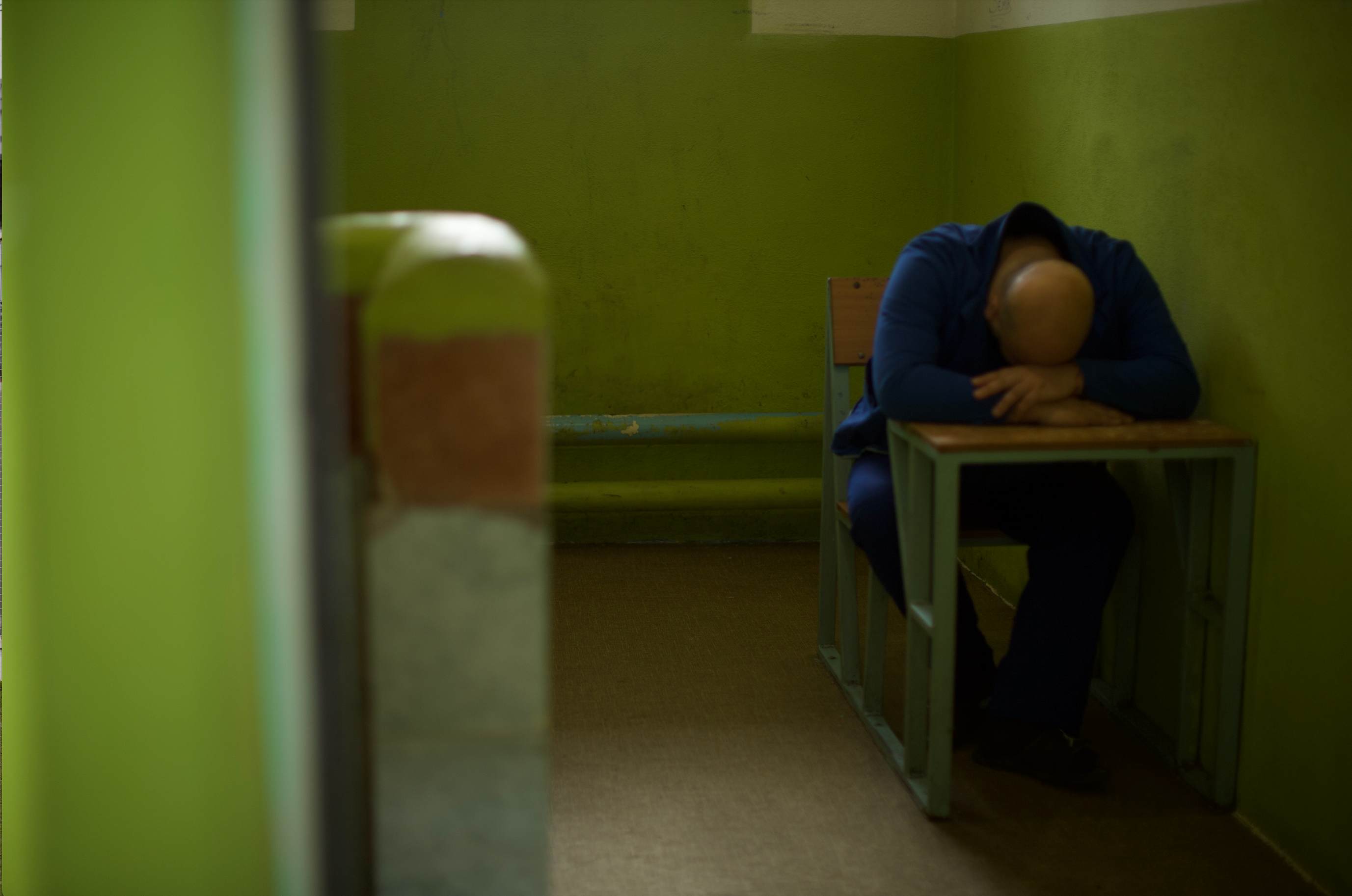 A person in blue clothing sitting at a desk in a prison cell, symbolizing the human impact of incarceration.