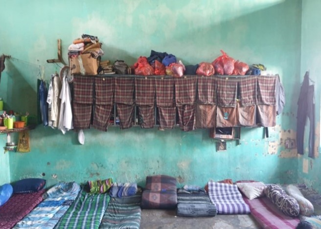 Overcrowded prison sleeping area with mattresses on the floor and makeshift storage